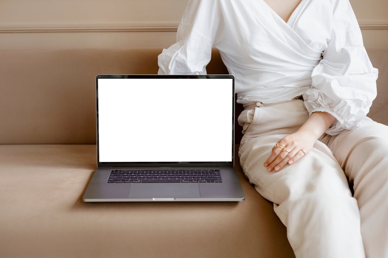 An adult sitting on a sofa with a blank laptop screen, ideal for mockups.